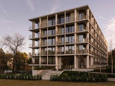 Moderní šestipodlažní hotelová budova s balkony, obklopená stromy a trávníky.