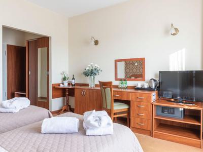 Camera d'hotel con due letti, mobili in legno, TV e scrivania in colori neutri.