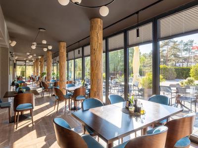 Zona pranzo luminosa con tavoli in legno, sedie e grandi finestre che si affacciano su terrazza e giardino.