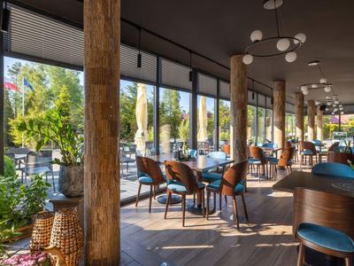 Terrazza di un hotel moderno con travi in legno, sedie blu e vista su un giardino soleggiato.