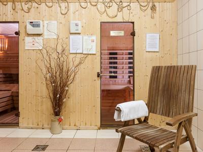 Sala sauna con sedie in legno, vaso con rami e informazioni sul muro.