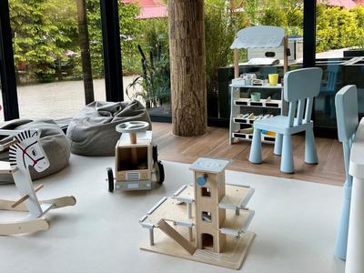 Area giochi per bambini con giocattoli in legno, sedie e ampie finestre che si affacciano sul verde.