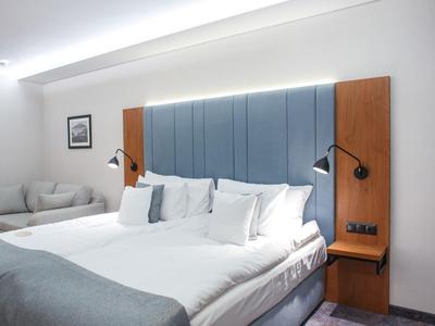 Camera d'hotel moderna con grande letto, testiera grigia e due lampade da lettura.