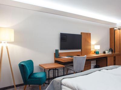 Camera d'hotel moderna con scrivania, sedia, TV e letto in primo piano.
