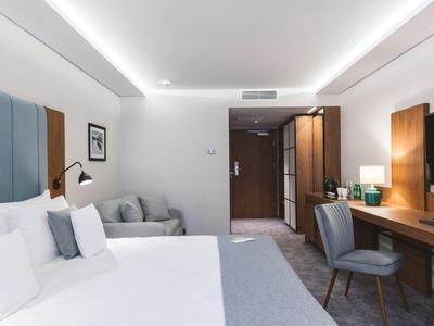 Camera d'hotel moderna con letto matrimoniale, scrivania, sedie comode e illuminazione soffusa.