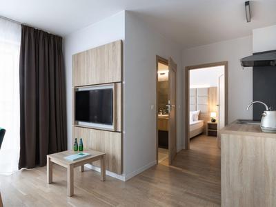 Area luminosa della camera d'hotel con pavimento in legno, TV, tavolo e vista su camera da letto e bagno.