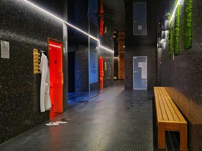Corridoio d'hotel moderno con pareti scure, porte rosse, panca in legno e piante verticali.
