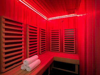 Sala sauna rossa con panchine in legno e tre asciugamani bianchi sulla panca.