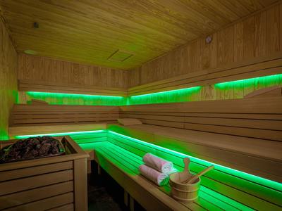 Sauna con pareti in legno, illuminazione LED verde e secchio con mestolo e asciugamani.