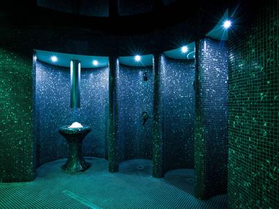 Area benessere scura con doccia e piccolo lavandino, illuminata da luci LED blu.