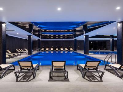 Hotel moderno con piscina interna illuminata e lettini in un ambiente elegante.