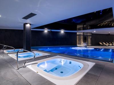 Piscina interna moderna con jacuzzi integrato e design del soffitto scuro in un hotel.