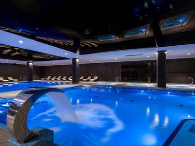 Piscina coperta moderna con cascata e illuminazione blu ambiente in un hotel.