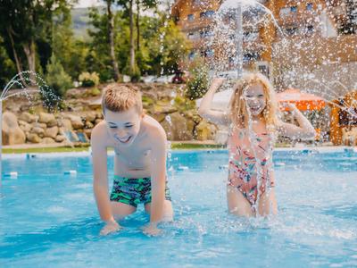 Due bambini giocano allegramente in una piscina con fontane d'acqua in una giornata di sole.
