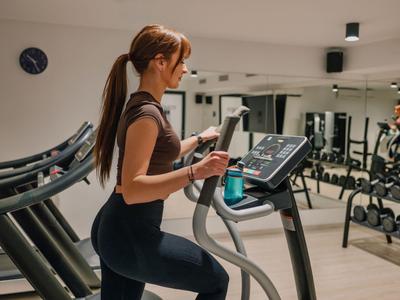 Donna che si allena su cross trainer in palestra di un hotel con specchi e manubri.