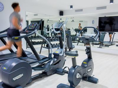 Sala fitness moderna con tapis roulant, cyclette e grandi specchi in un interno luminoso.