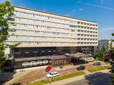 Edificio alberghiero su più piani con facciata in vetro e auto sulla strada davanti.