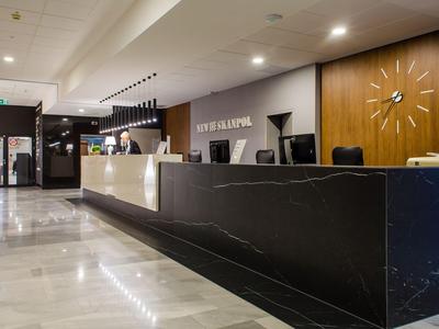 Reception moderna di un hotel con banco nero, area soggiorno e orologio a parete.