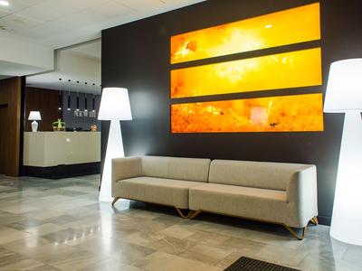 Lobby di un hotel moderno con divano beige, lampade da terra bianche e arte murale gialla a tre pezzi.