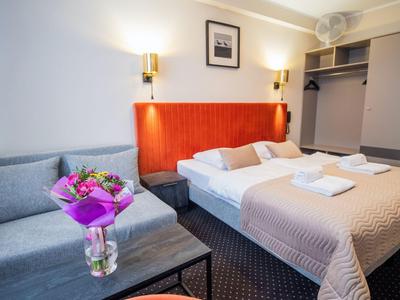 Camera d'hotel moderna con letto matrimoniale, divano grigio, mazzo di fiori e armadio aperto.