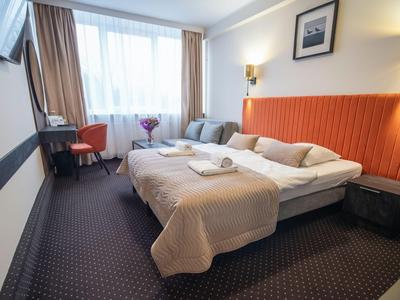 Camera d'hotel accogliente con letto matrimoniale, scrivania, sedia e grande finestra con tende.