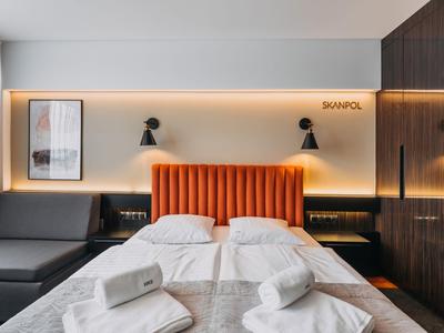 Camera d'hotel moderna con letto matrimoniale, testiera arancione e illuminazione elegante.