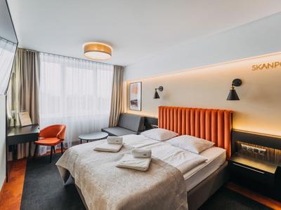 Camera d'hotel moderna con letto matrimoniale, testiera arancione e finestra con tende.