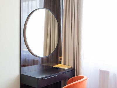Area hotel moderna con specchio rotondo, tavolo nero e sedia arancione vicino a finestra luminosa.