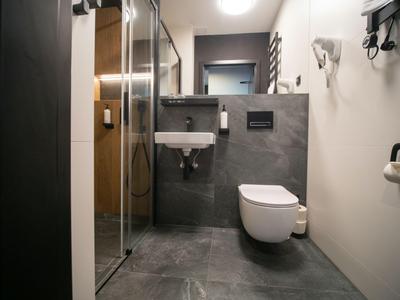 Bagno d'hotel moderno con cabina doccia, wc a muro e piccolo lavandino.