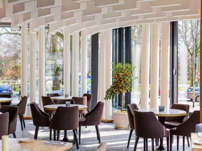 Ristorante moderno dell'hotel con sedie marroni e grandi finestre che affacciano su un parcheggio alberato.