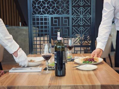 Due camerieri servono piatti a un tavolo di legno in un ristorante elegante.