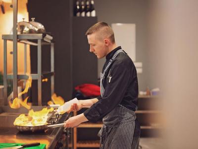 Uno chef in cucina che crea fiamme con una padella.