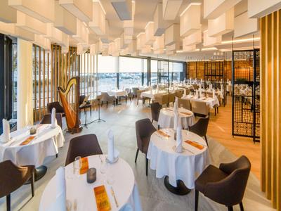 Ristorante moderno con tovaglie bianche e vista sull'acqua attraverso grandi finestre.