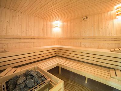 Sauna luminosa con panche in legno e stufa con pietre calde in un angolo.