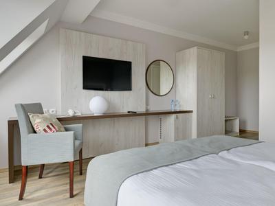 Habitación de hotel moderna con TV, escritorio, silla y cama cómoda en tonos neutros.