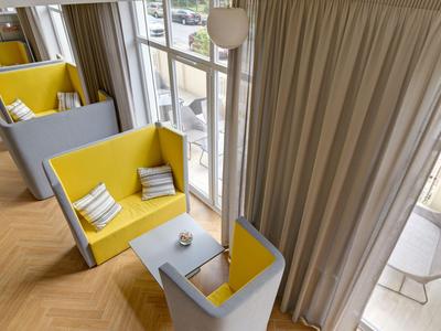 Área de asientos con muebles tapizados amarillos y grises junto a ventanas de piso a techo en un hotel.