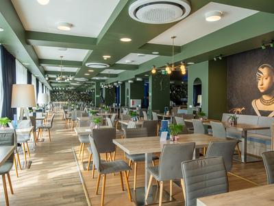 Comedor moderno con sillas de madera, mesas y acentos verdes en el techo en un hotel.