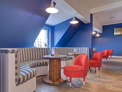 Área de salón moderna en hotel con paredes azules, sillones rojos y bancos curvos.