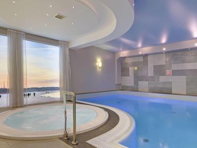 Piscina cubierta moderna con jacuzzis y grandes ventanas al atardecer en un hotel.