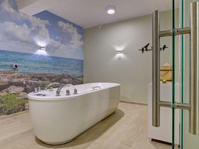 Baño de hotel moderno con bañera independiente y un mural de paisaje costero.