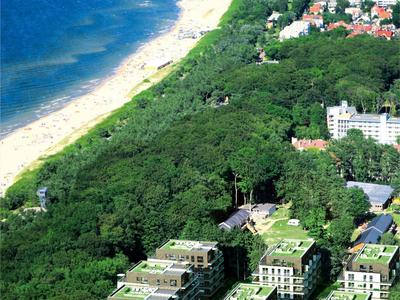 Vue aérienne d'une station balnéaire avec plage, forêt et bâtiments modernes.