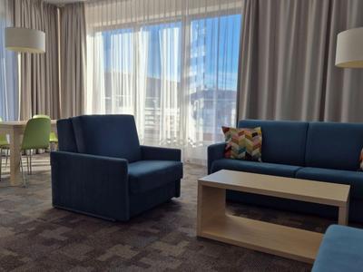 Chambre d'hôtel lumineuse avec des fauteuils bleus, un canapé, une table et un bureau avec chaise près de la fenêtre.
