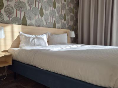 Chambre d'hôtel moderne avec grand lit, tables de nuit, lampes et mur à motifs.