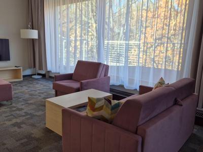 Chambre d'hôtel confortable avec coin salon, télévision et grandes fenêtres avec rideaux.