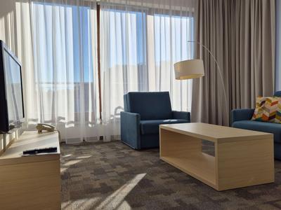 Chambre d'hôtel lumineuse avec grandes fenêtres, sièges bleus et table basse au centre.