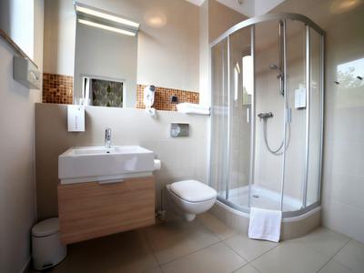 Salle de bain moderne avec douche, lavabo, toilettes et carreaux clairs.
