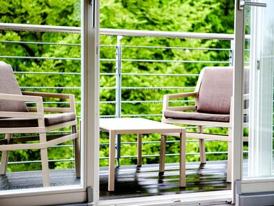 Balcon avec deux chaises rembourrées et une petite table en bois face à des arbres verts.
