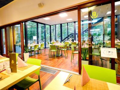 Salle à manger lumineuse et moderne avec grandes fenêtres et chaises vertes dans un hôtel.
