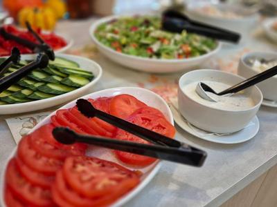 Buffet de salade frais avec tomates, concombres, salade et vinaigrettes dans des bols blancs.