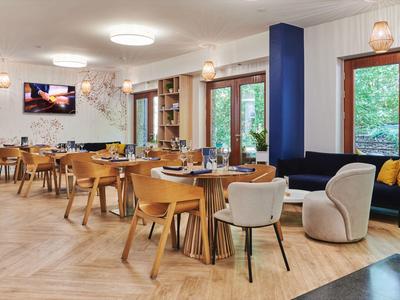 Salle à manger moderne avec tables en bois, chaises et grande fenêtre dans un hôtel.